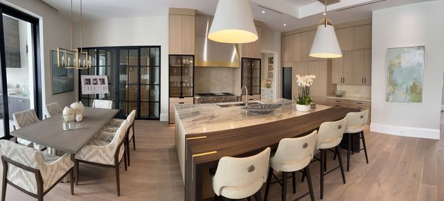 Modern open-plan dining and kitchen area with long table, white chairs, pendant lights, and glass cabinets