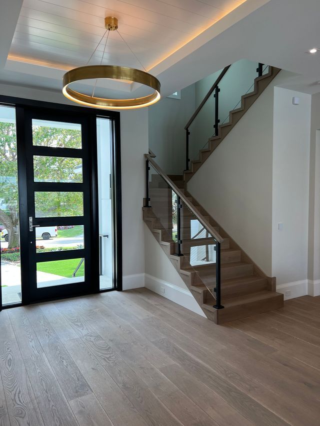 Modern entryway with black front door, floating staircase, and round ceiling light on wood flooring