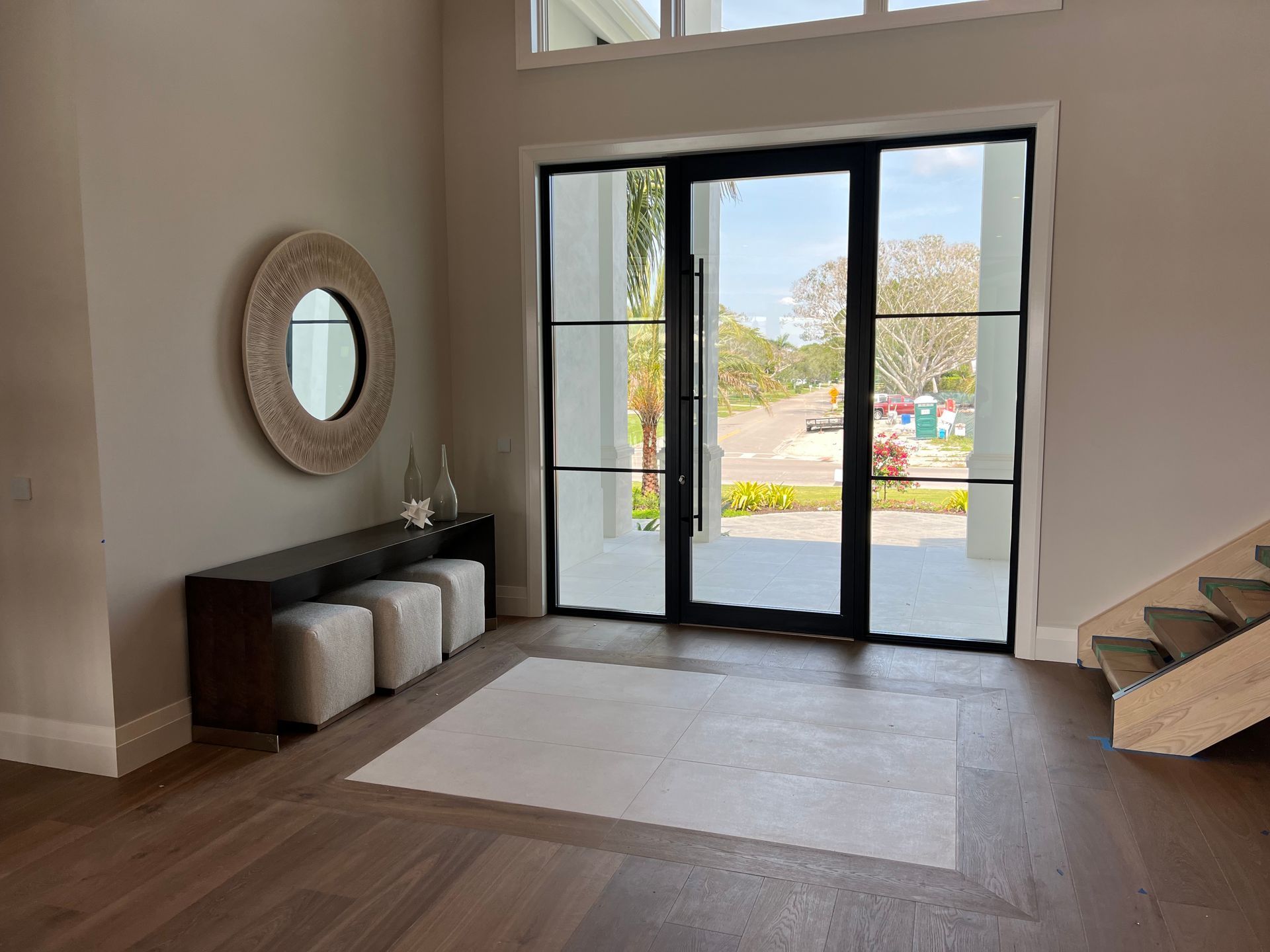 Modern foyer with bench, round mirror, wood floor, and glass double doors to outside