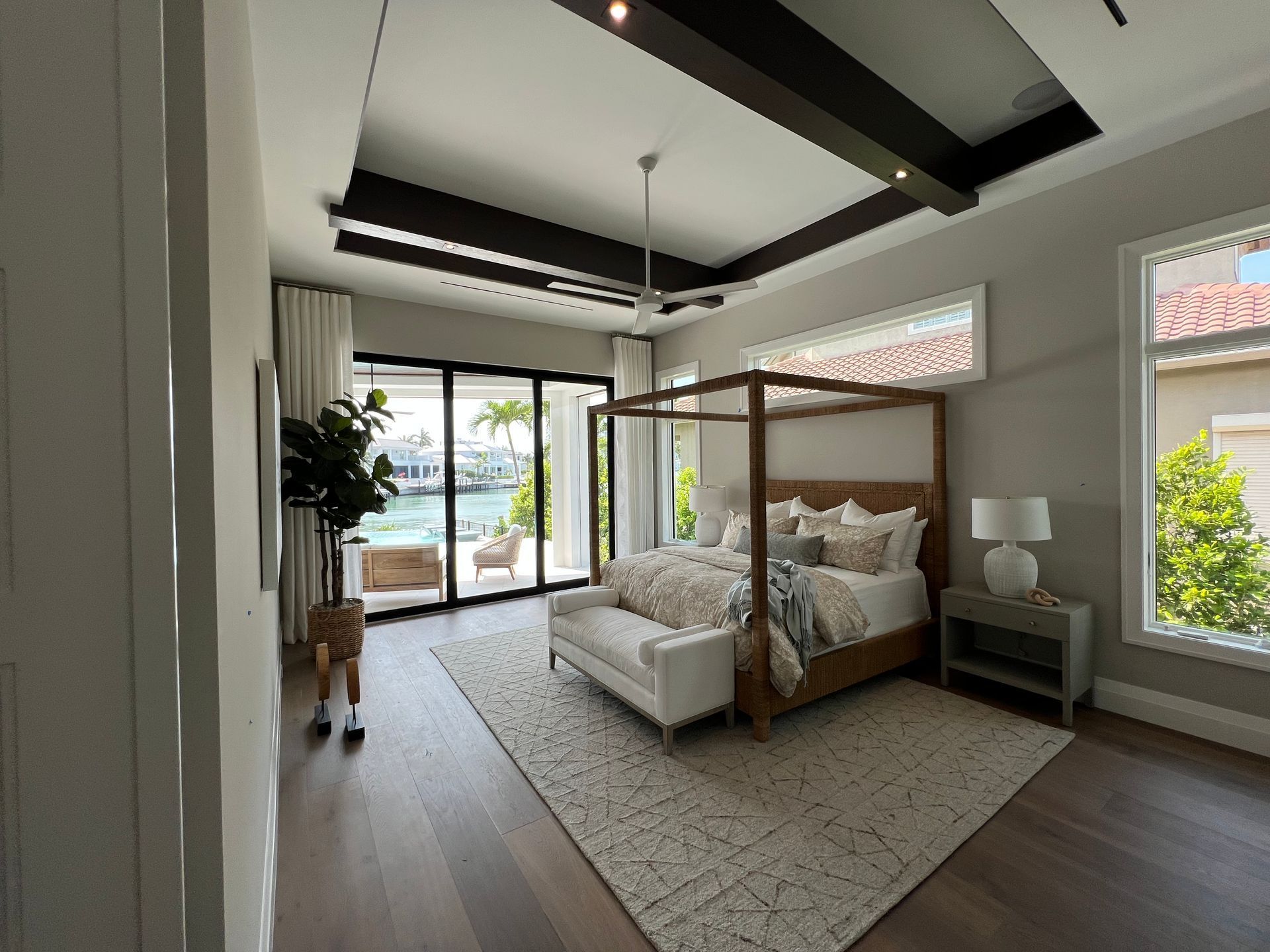 Bright modern bedroom with canopy bed, large windows, and sliding glass doors opening to a patio.