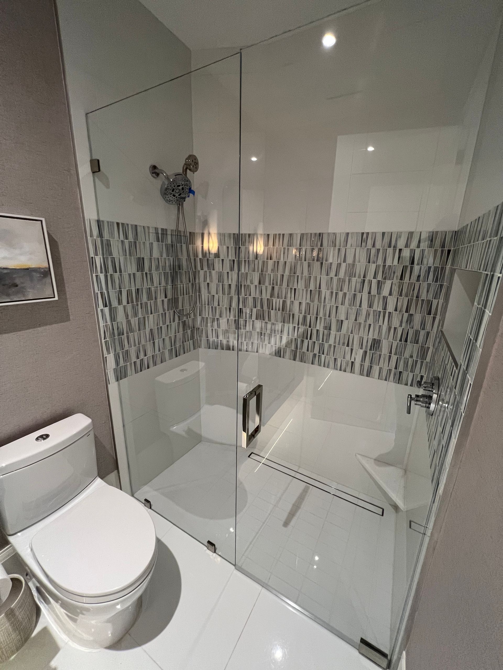 Modern bathroom with a toilet, glass walk-in shower, and mosaic tile accent wall