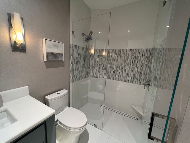 Modern bathroom with toilet, sink, glass shower enclosure, and gray tile accents