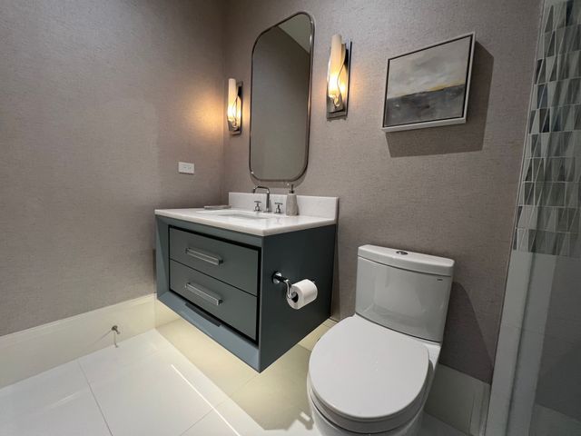 Modern bathroom with floating vanity, mirror, wall lights, and a toilet on white tile floor