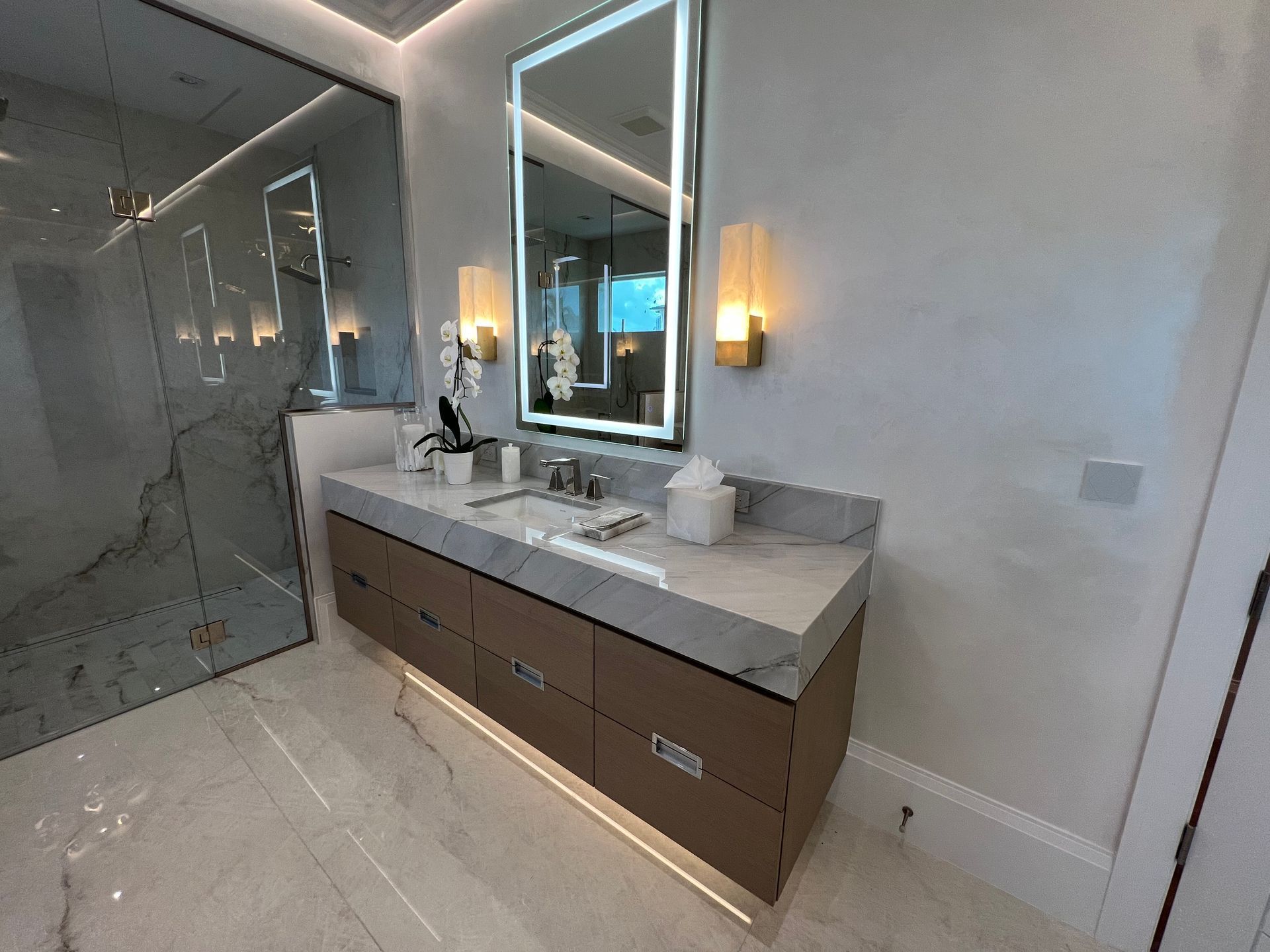 Modern bathroom vanity with double sinks, large mirror, and marble tile shower.
