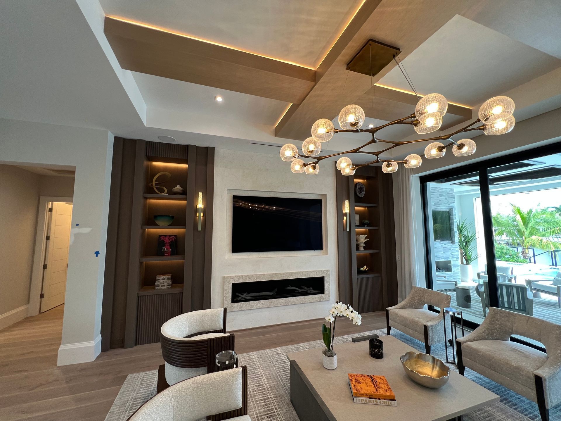Modern living room with built-in shelves, a wall-mounted TV, and a large chandelier over a coffee table.