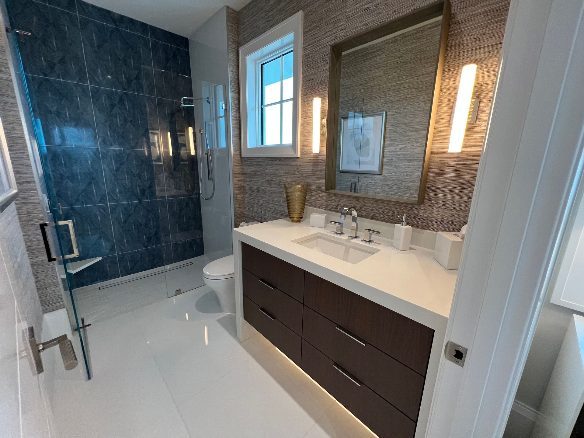 Modern bathroom with dark blue tiled shower, floating vanity, and large mirror