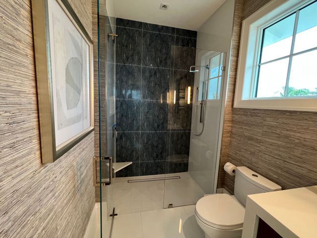 Modern bathroom with glass shower, toilet, vanity, and window on the right