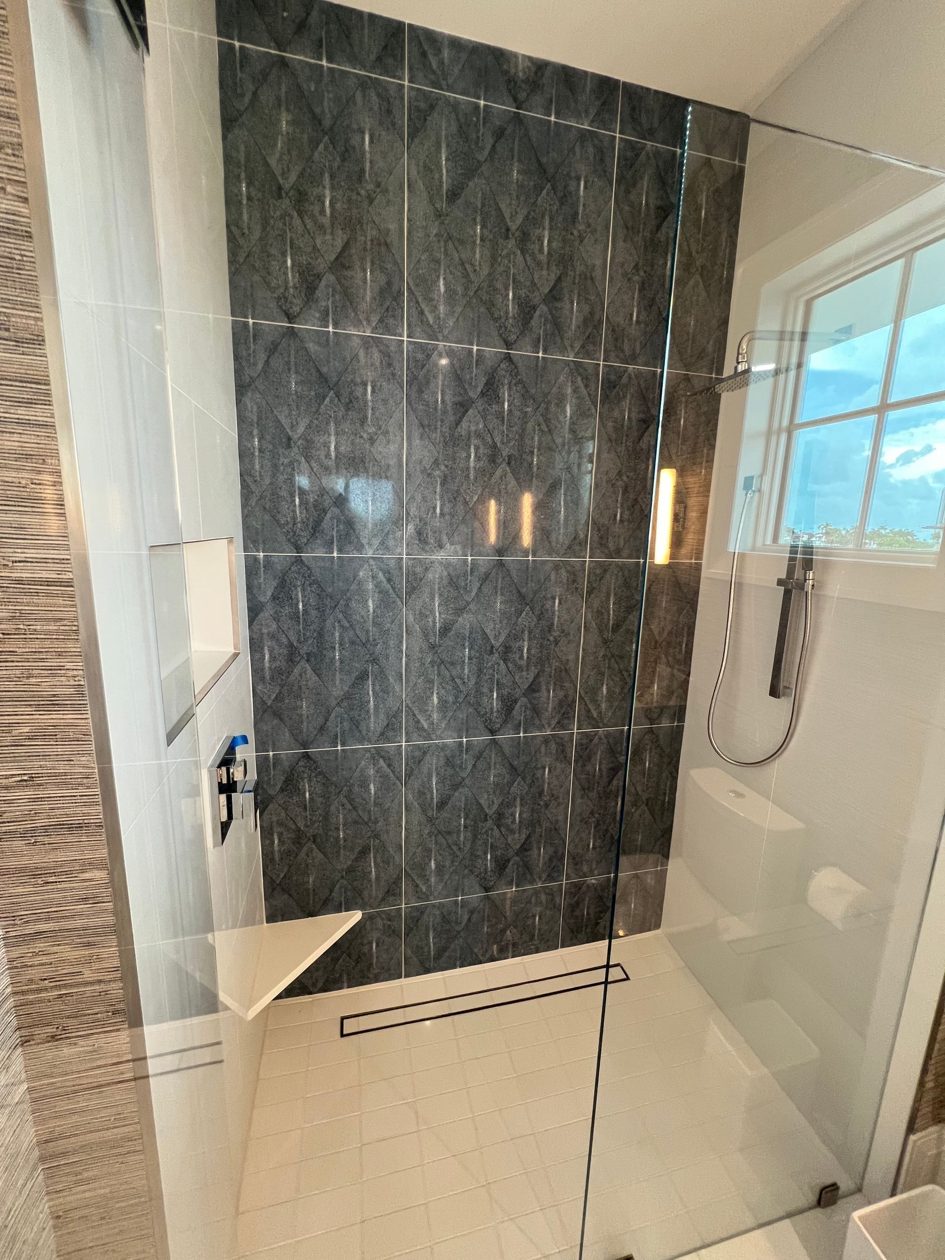 Modern bathroom shower with dark marble tile, glass door, and beige walls