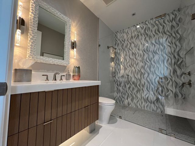 Modern bathroom with floating vanity, mirror, white fixtures, and gray patterned shower wall.