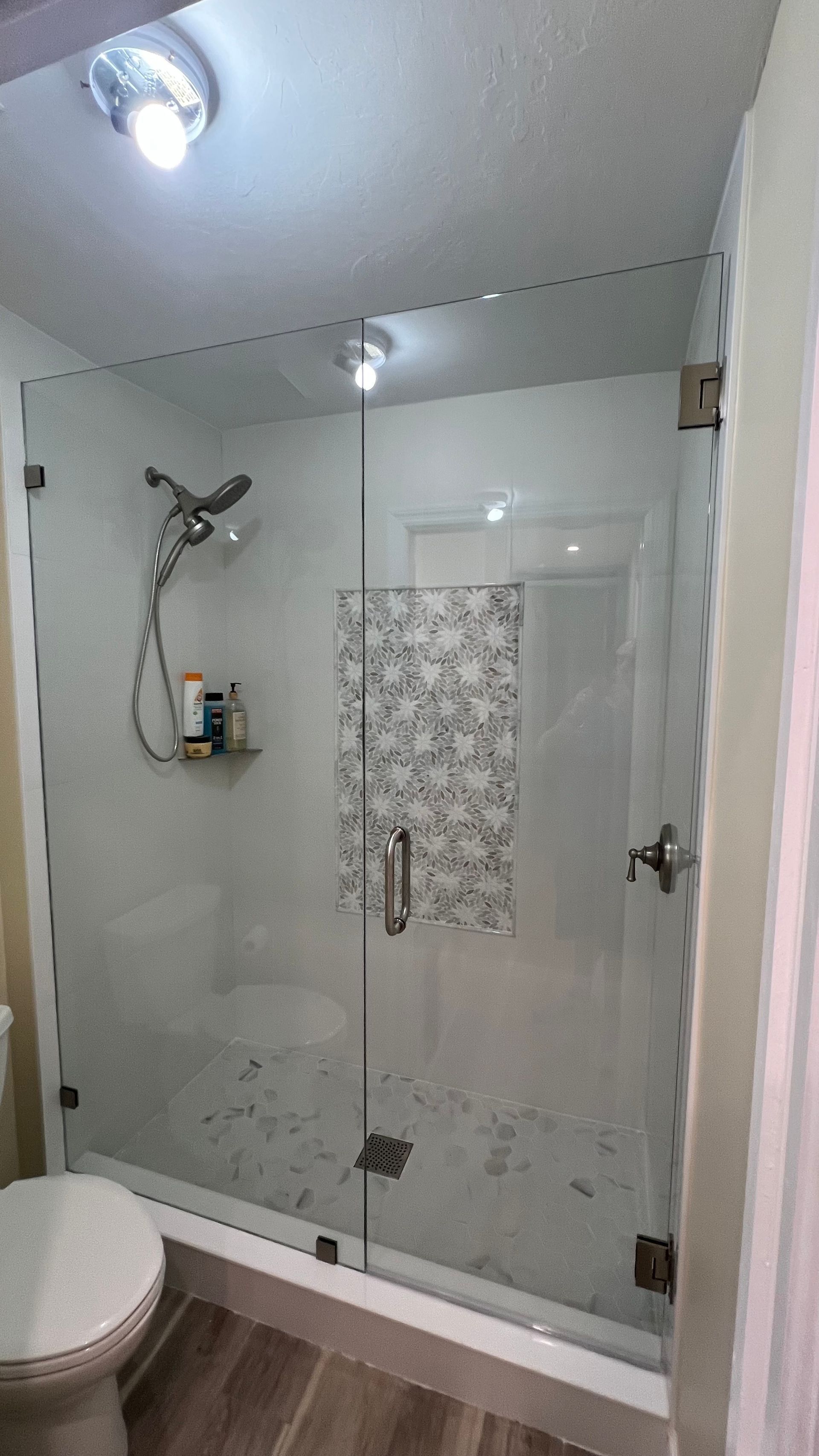 Small bathroom with a glass-enclosed shower, patterned tile accent, and toilet visible on the left.