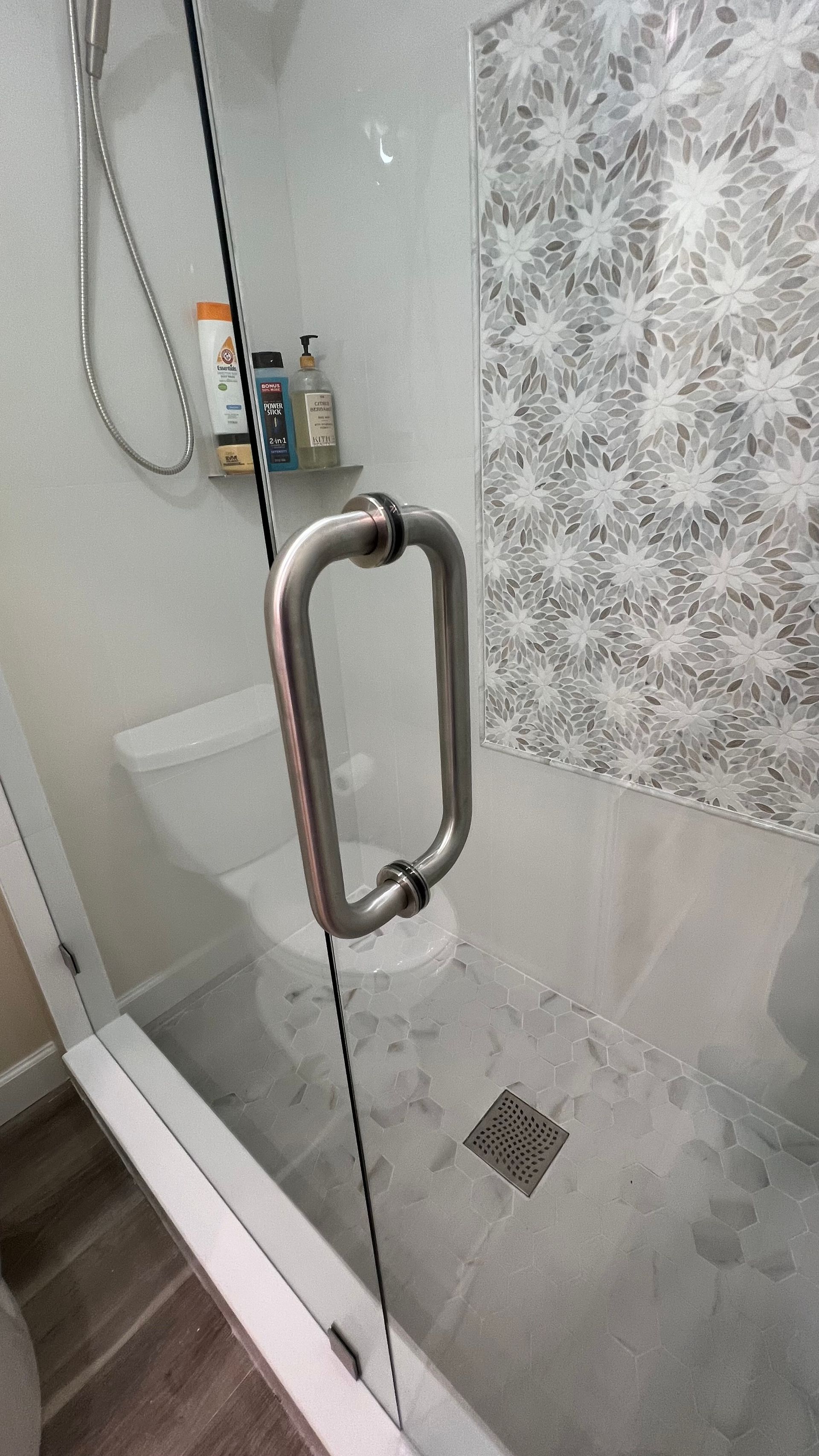 Glass shower door with metal handle and tiled bathroom interior
