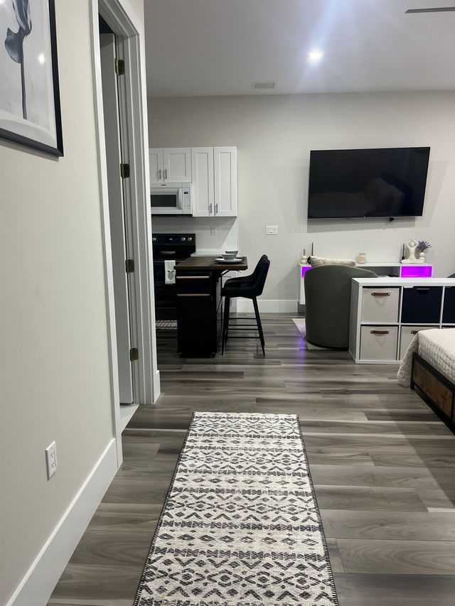 Modern apartment living area with hallway, kitchen nook, wall TV, couch, and patterned runner rug