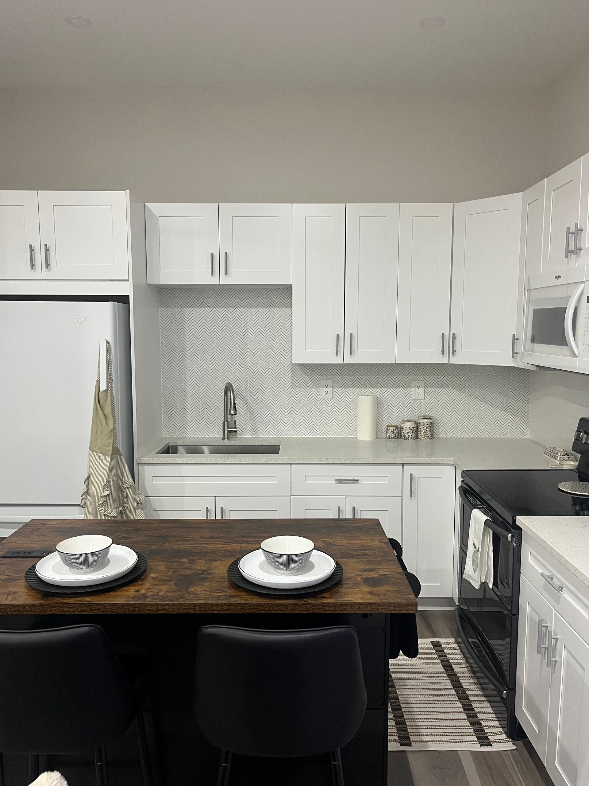 Modern kitchen with white cabinets, stainless appliances, and a dark wood dining table with place settings