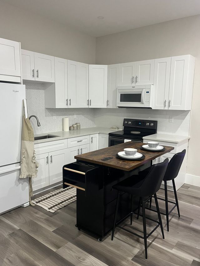 Bright white kitchen with dark island, stools, and place settings under white cabinets