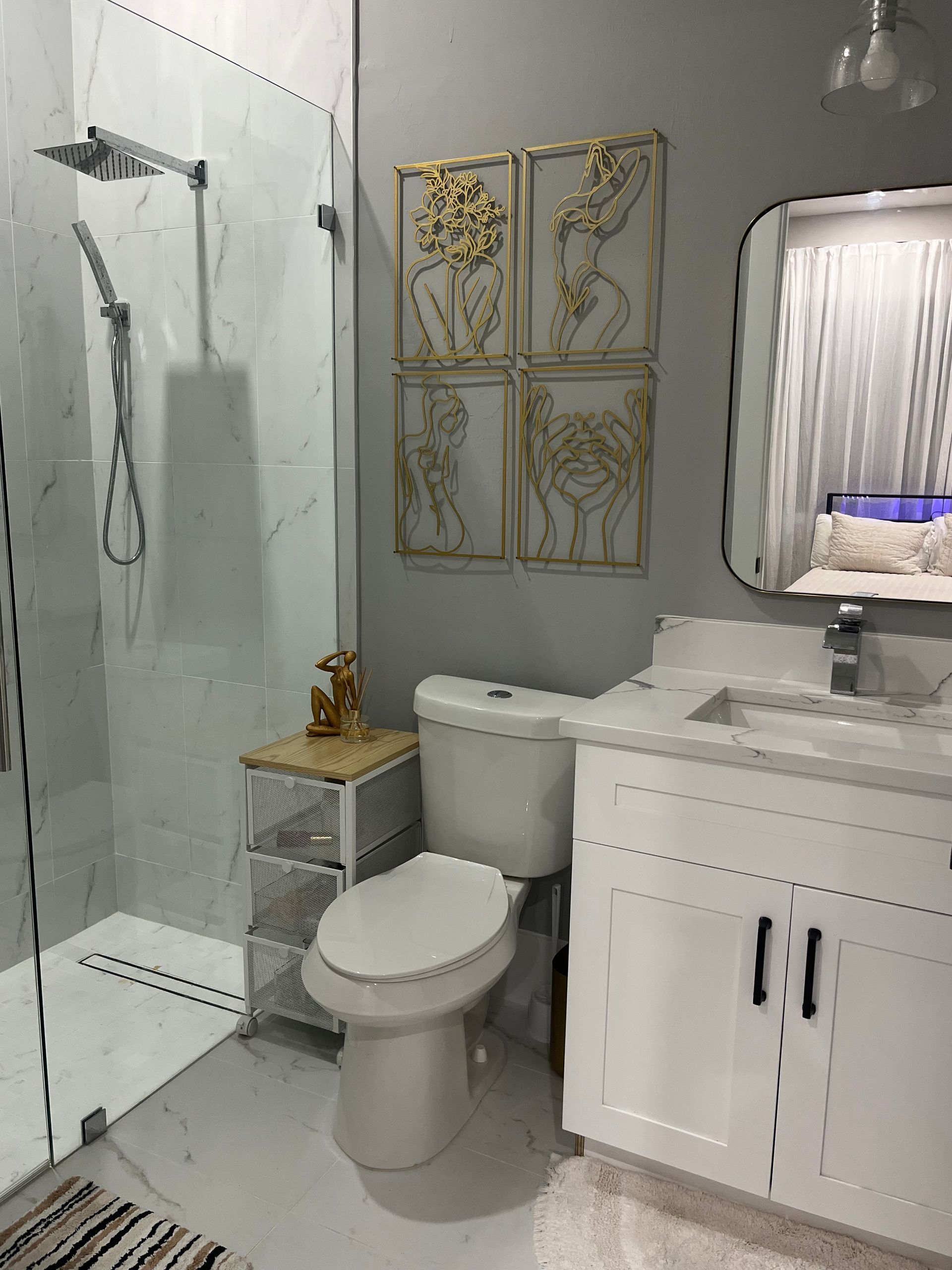 Modern bathroom with glass shower, toilet, white vanity, and gold wall decor.