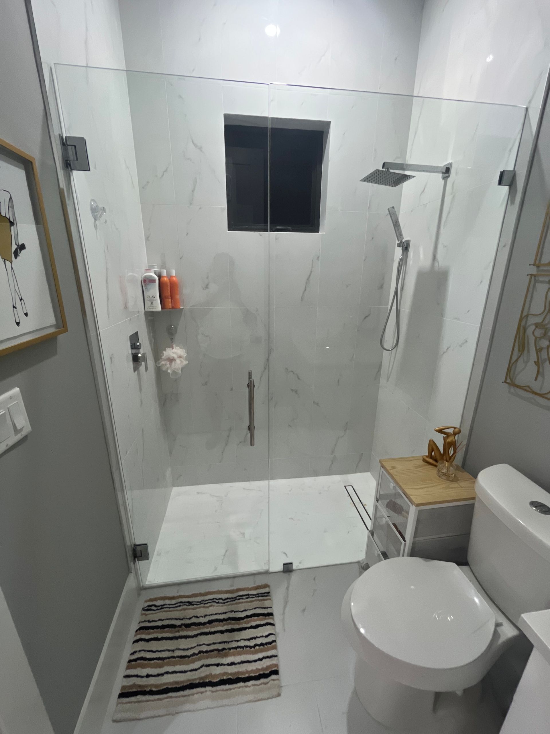 Small bathroom with glass shower, toilet, and striped rug.