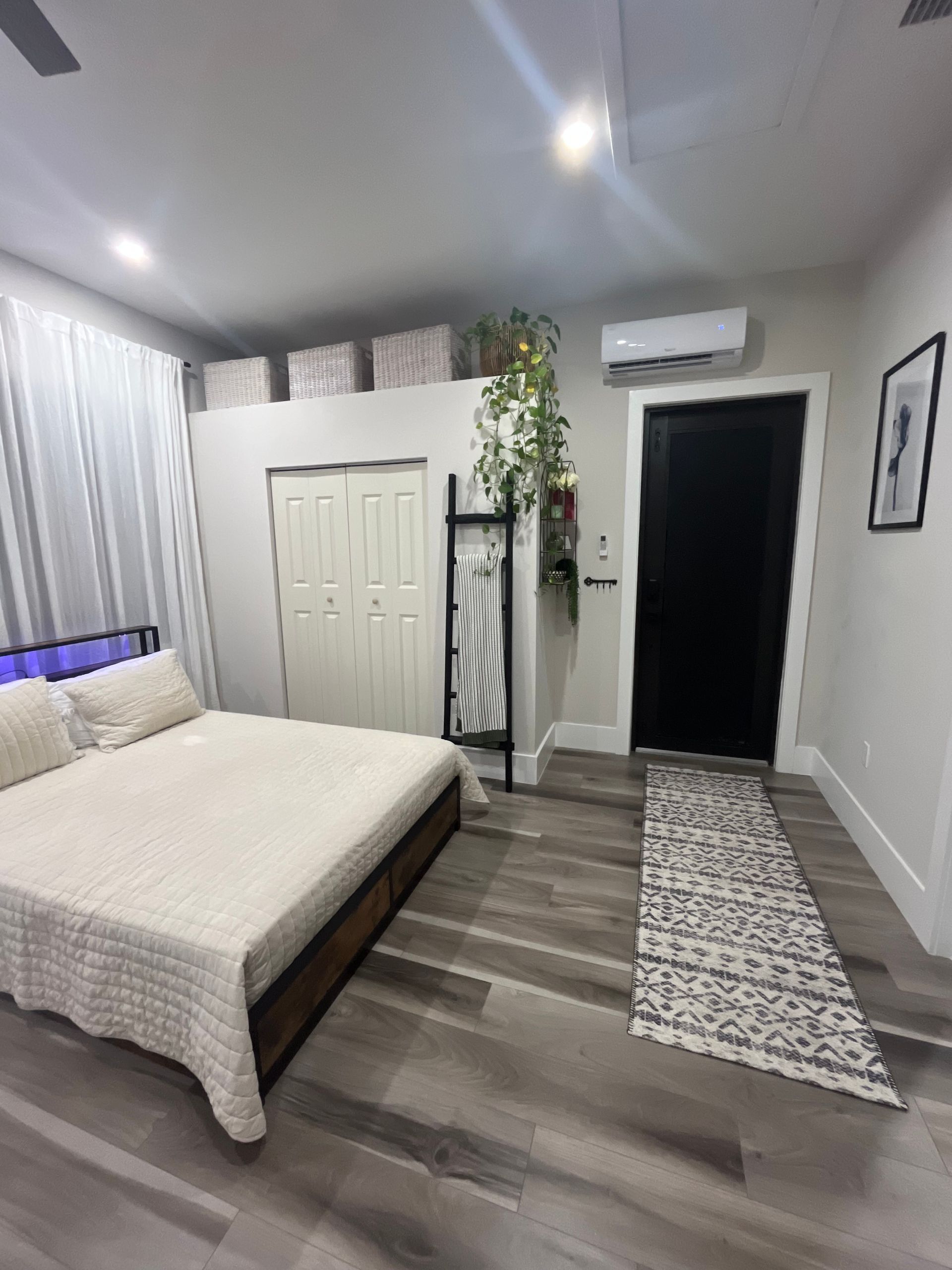 Bright bedroom with a bed, closet, rug runner, lamp, and wall art on gray floors.
