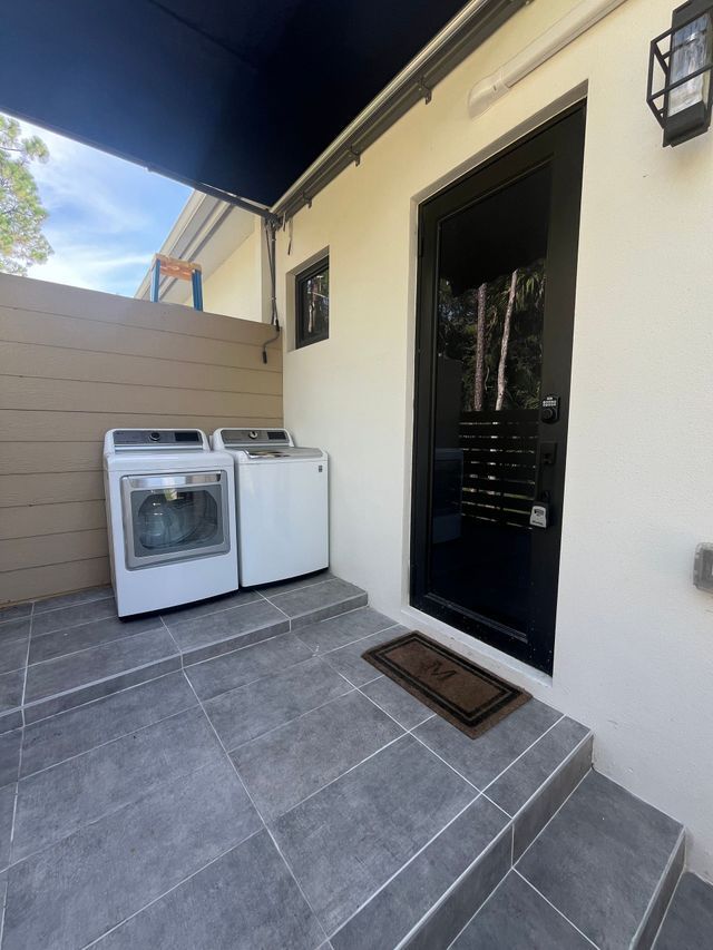 Laundry area beside a black door, with a washer, dryer, and gray tiled steps under a covered patio