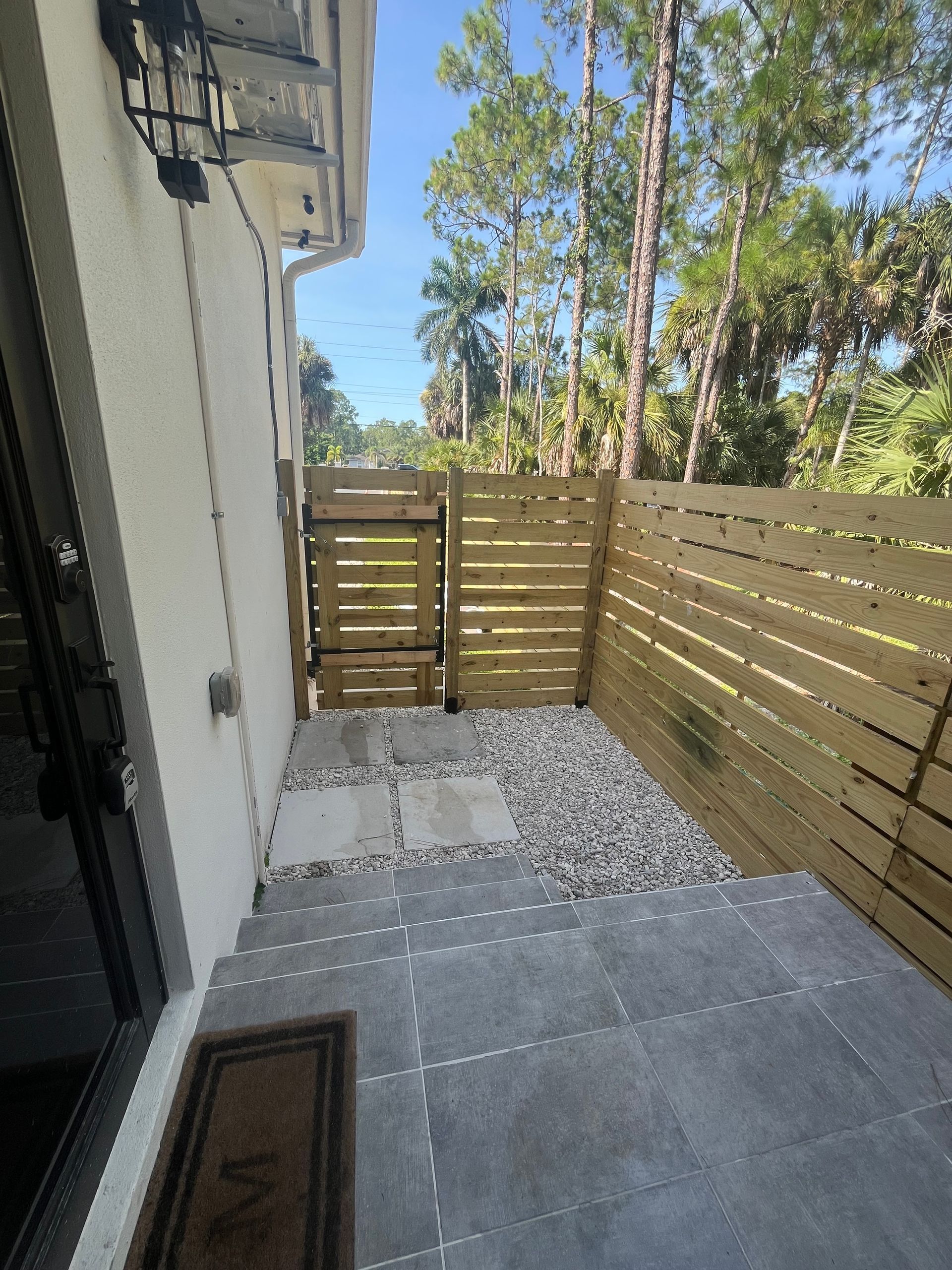 Small patio with gray tiles, white gravel, and a wooden privacy fence beside a house.