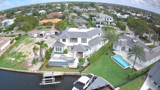 Aerial view of waterfront homes with docks, boats, and a backyard pool in a sunny neighborhood