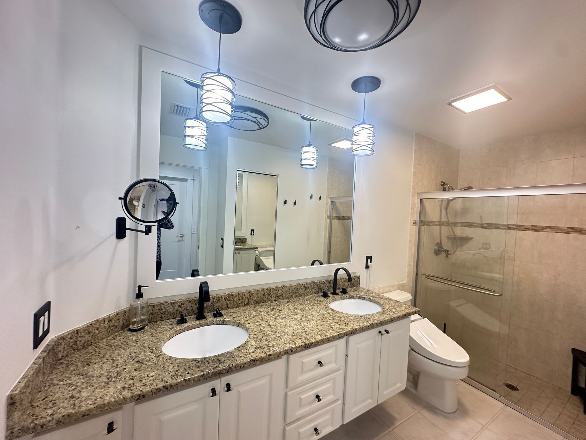 Spacious bathroom vanity with granite countertop, double sinks, large mirror, and glass-enclosed shower.