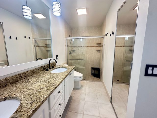 Bright modern bathroom with granite vanity, double mirrors, walk-in shower, and beige tile floor
