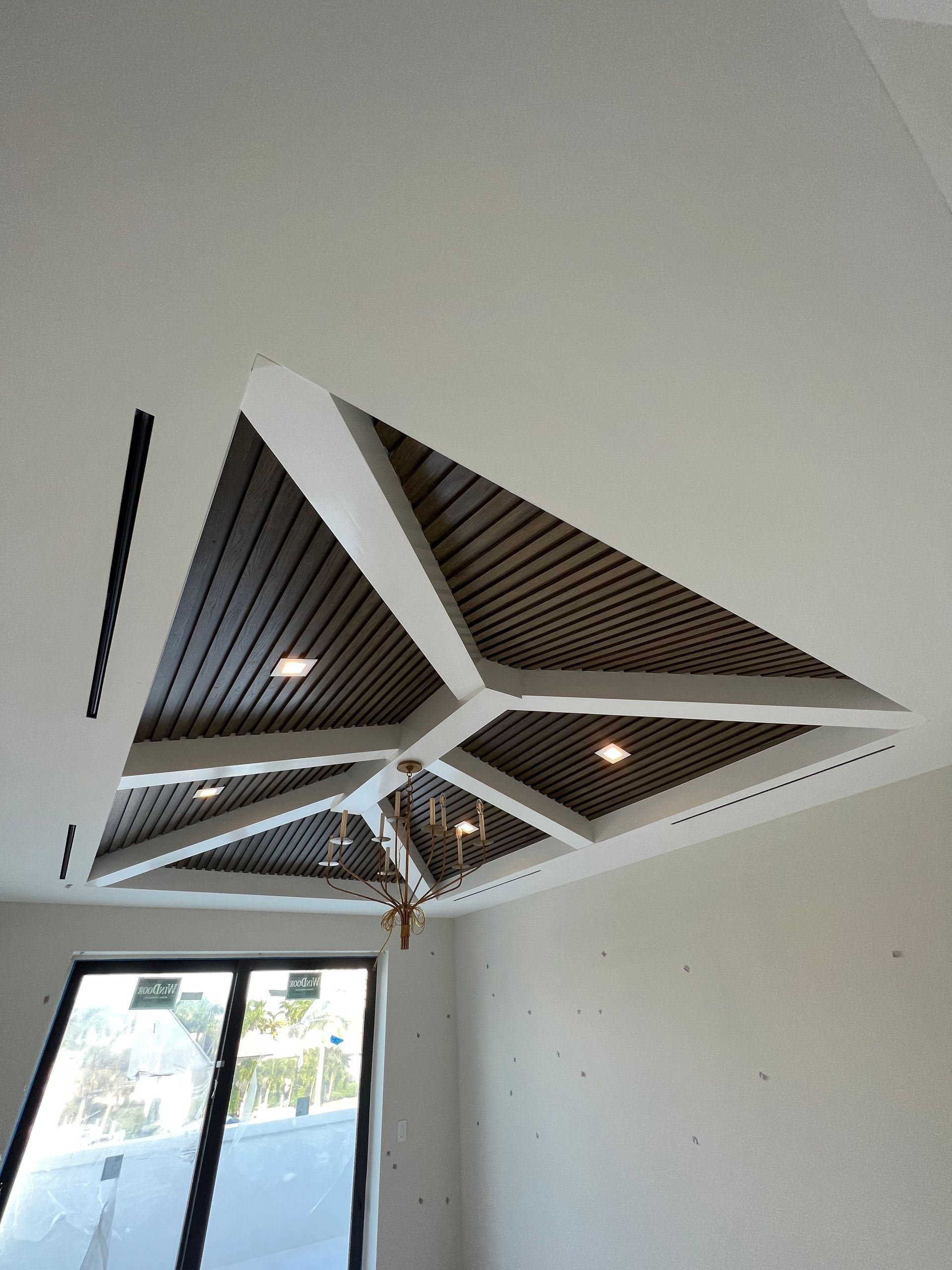 Modern ceiling with dark wood slats, white beams, and recessed lights above a room with large windows