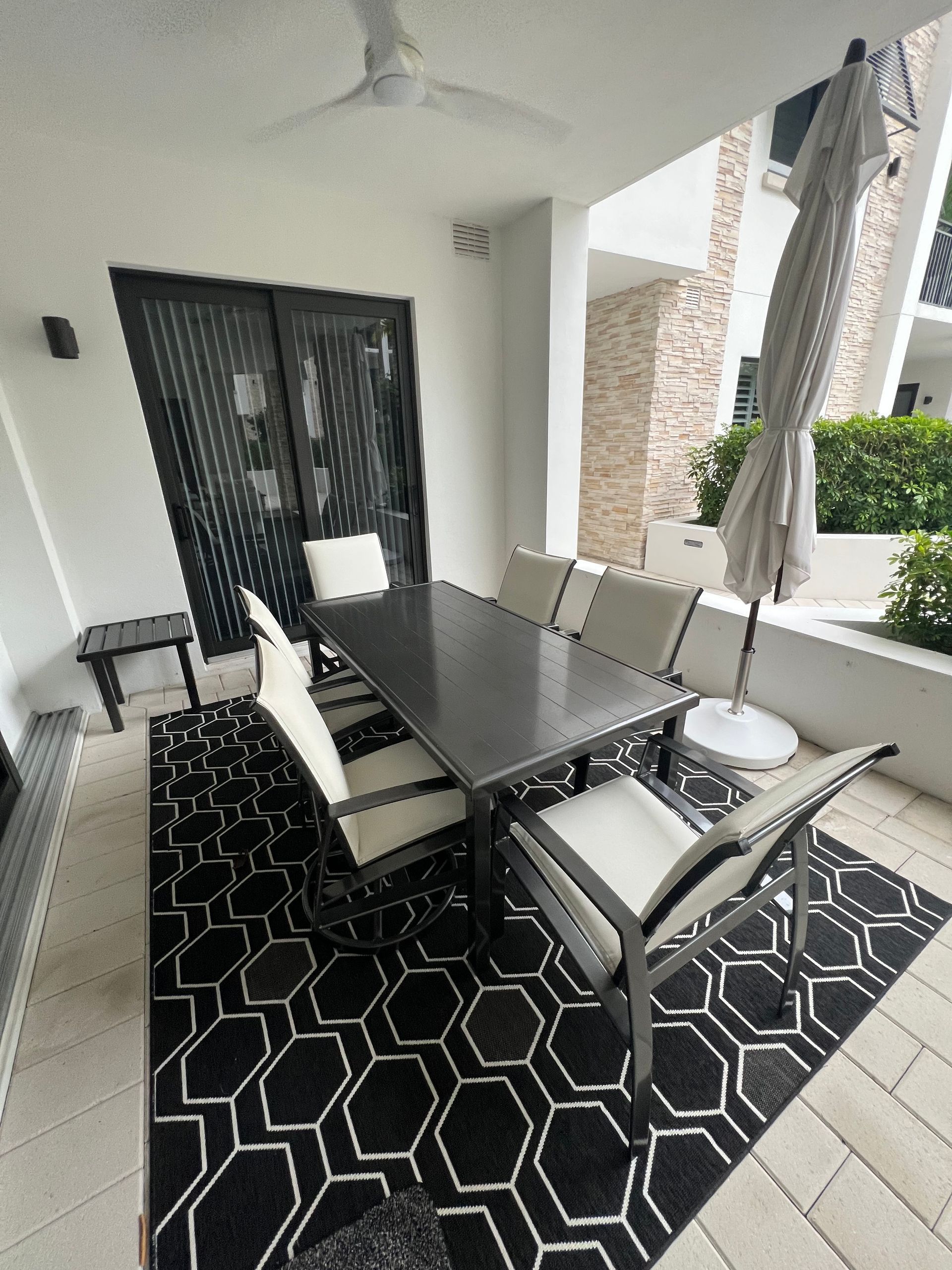 Covered patio dining area with black table, gray chairs, and geometric black rug