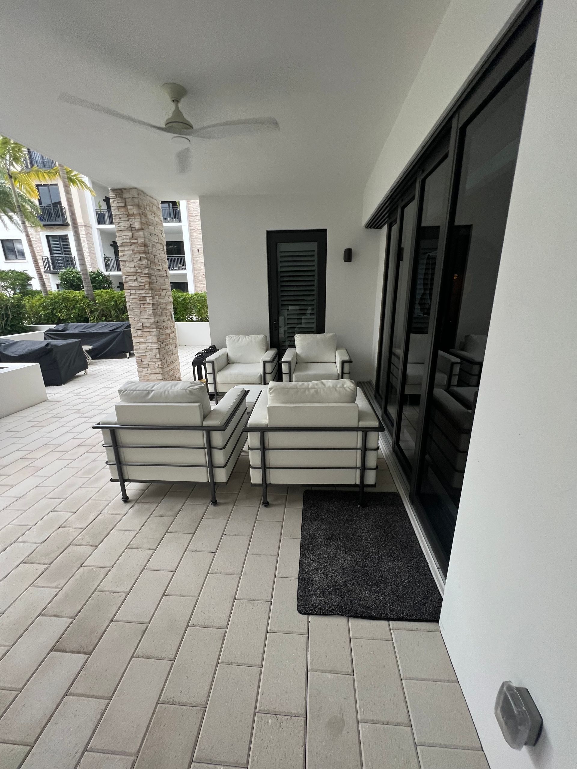 Covered patio with white cushioned chairs, glass table, potted plants, and black sliding doors