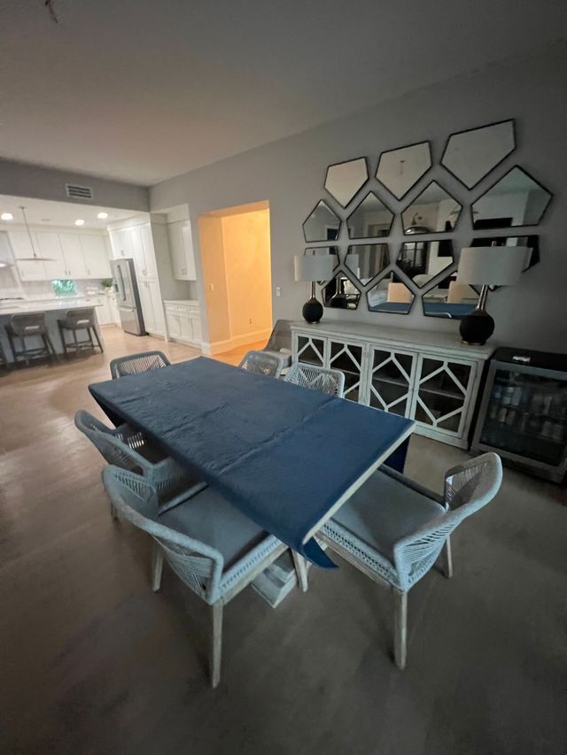 Modern dining room with a blue table runner, gray chairs, mirrored wall decor, and a lit doorway.