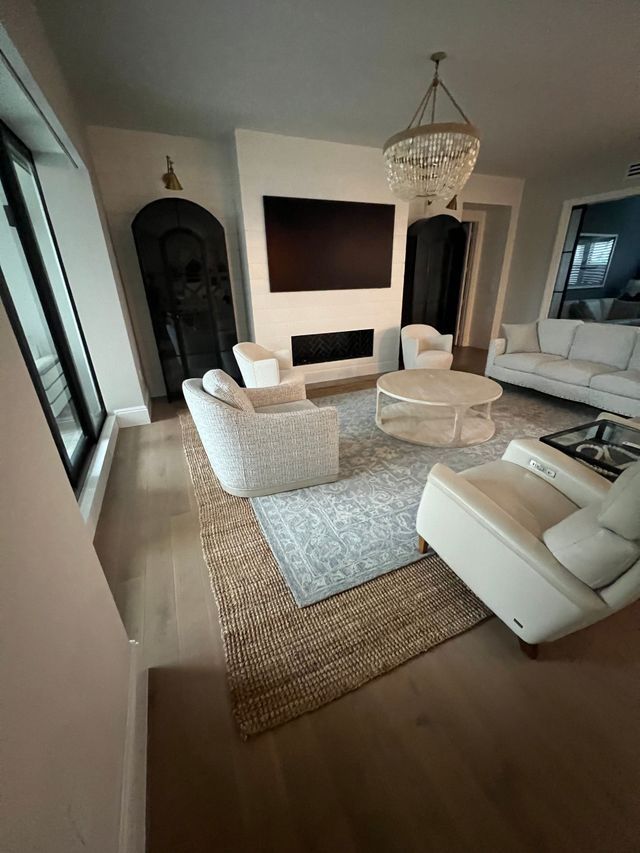 Elegant living room with white seating, chandelier, fireplace, and large wall-mounted TV