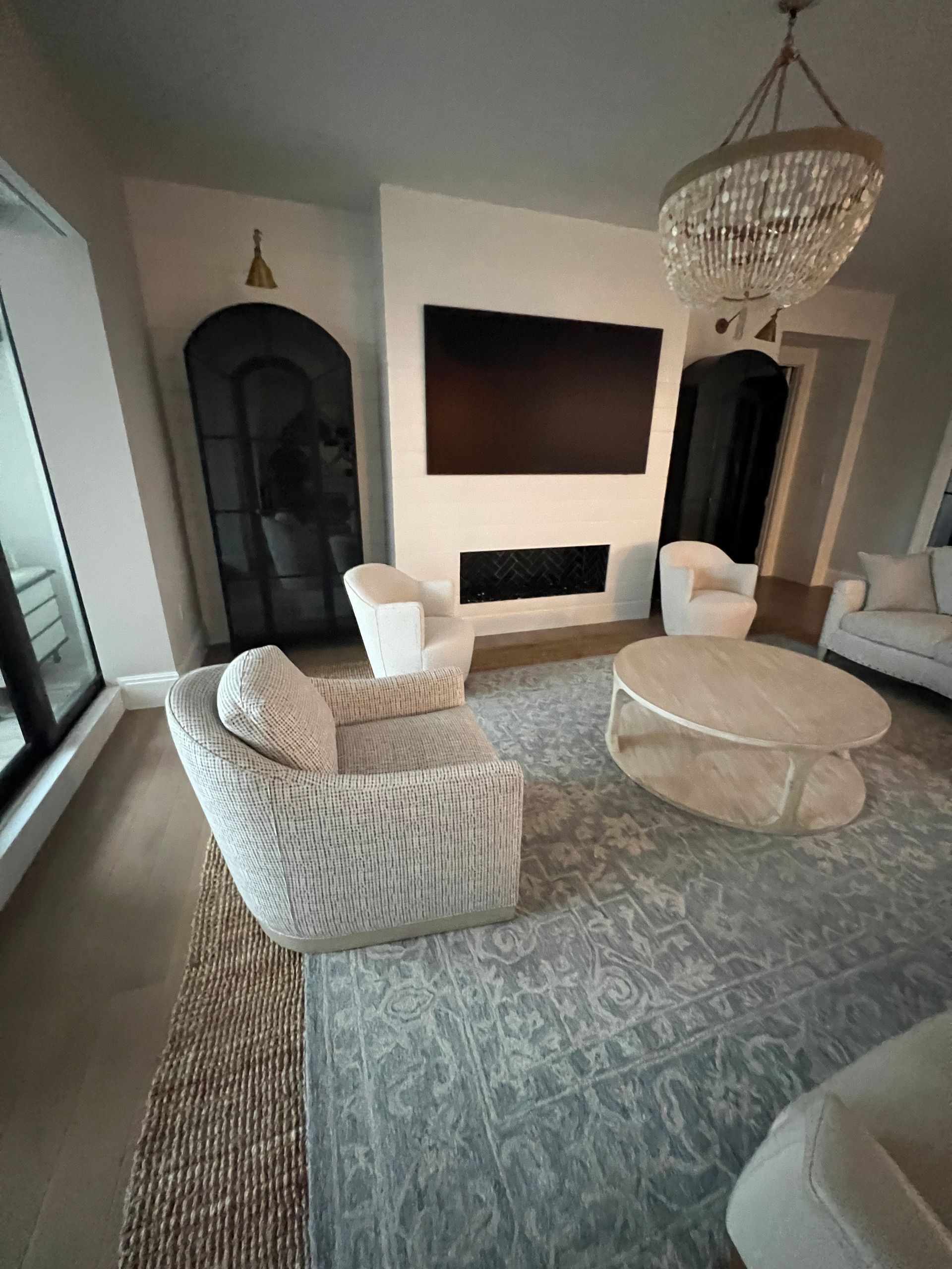 Elegant living room with chandelier, large wall-mounted TV, patterned rug, and plush cream seating