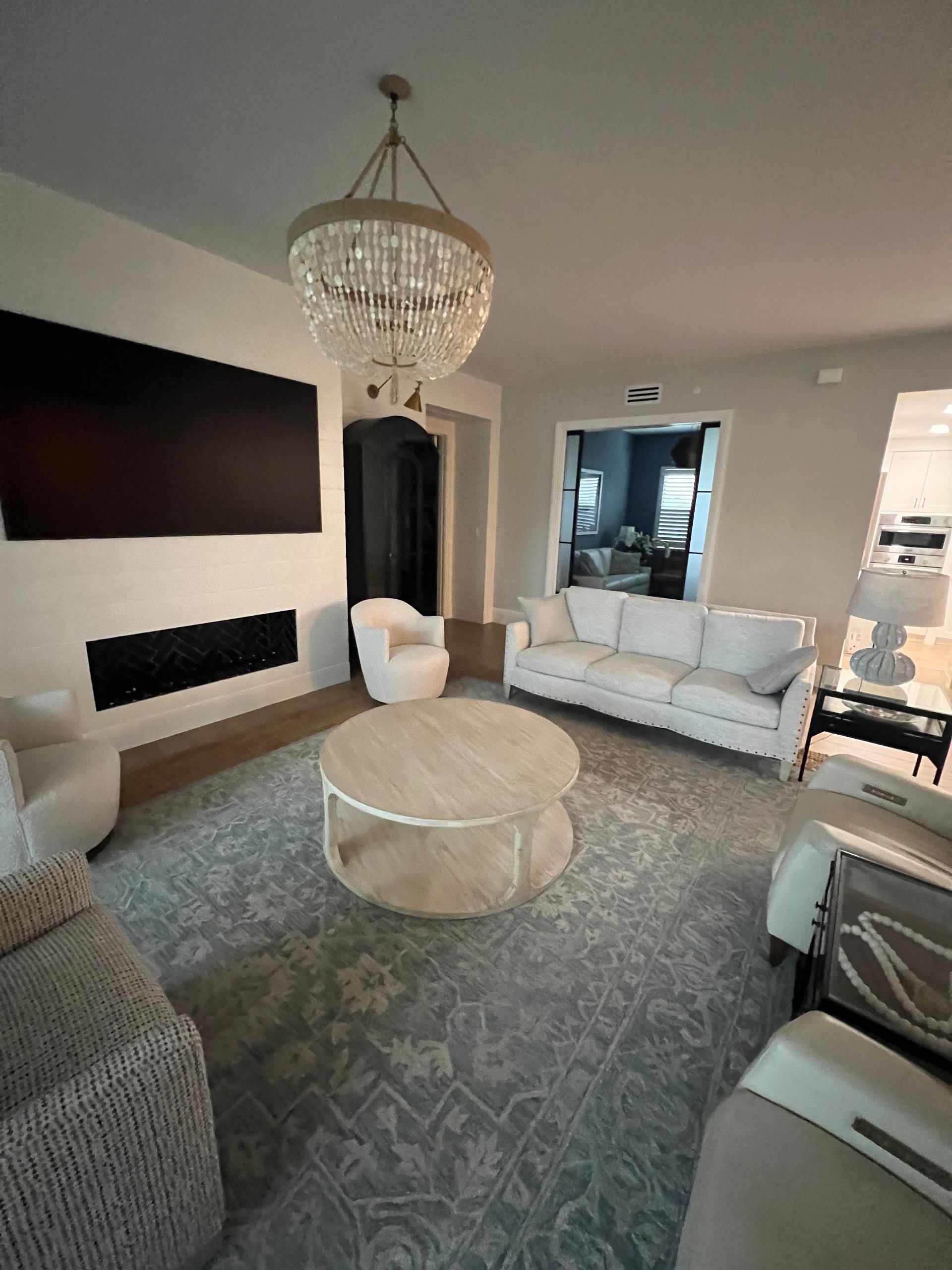 Elegant living room with gray sofas, round coffee table, chandelier, and patterned rug.