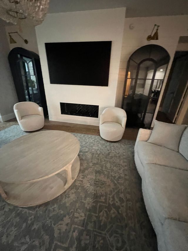 Modern living room with fireplace, large TV, round coffee table, two white chairs, and a gray sofa