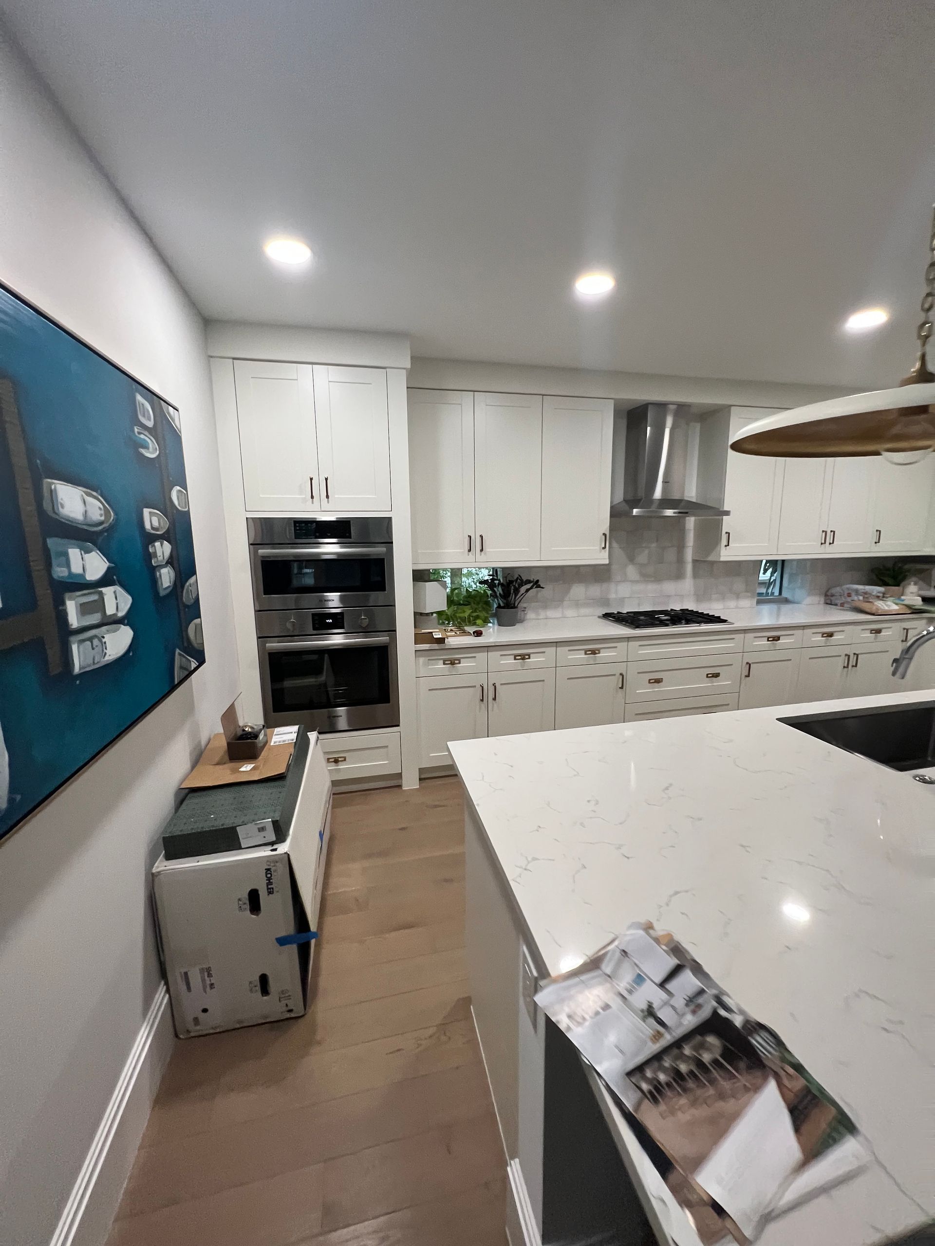 Bright modern kitchen with white cabinets, island, stainless appliances, and wood floor.