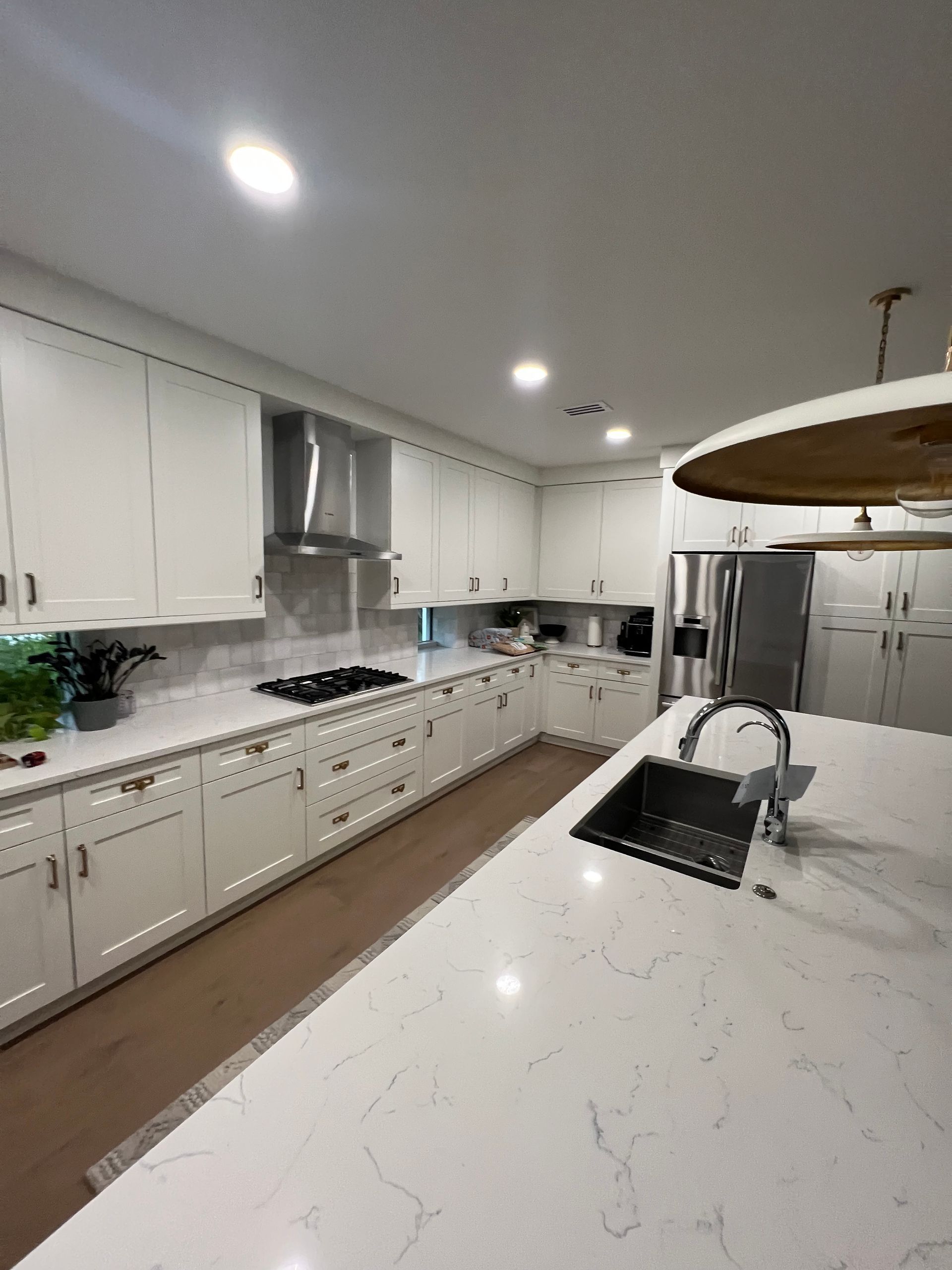 Bright modern white kitchen with marble countertops, island sink, and stainless steel appliances