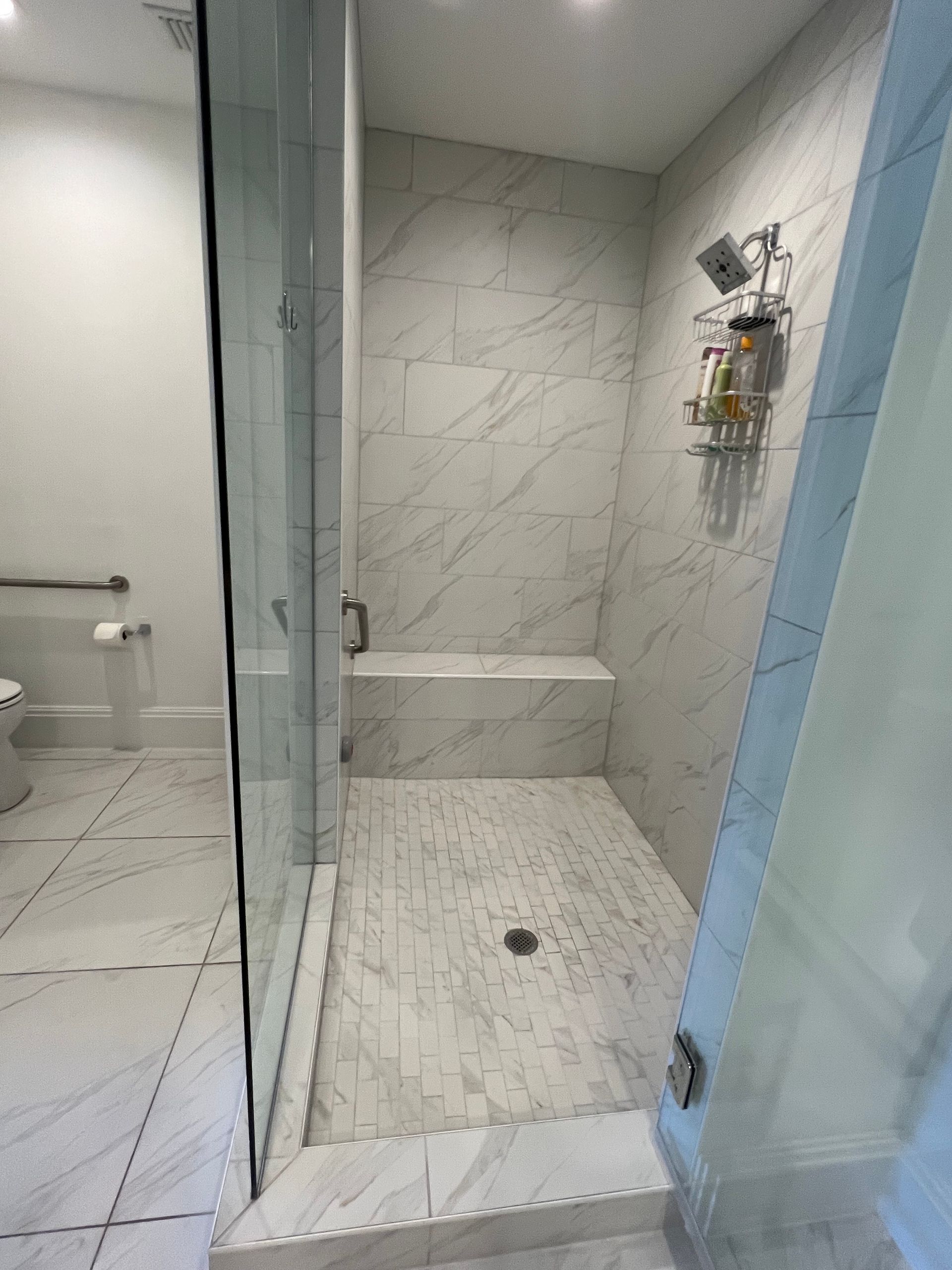 Modern tiled walk-in shower with glass door, built-in bench, and showerhead niche.