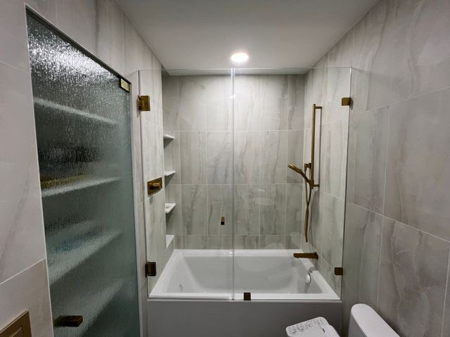Accessible bathroom with walk-in tub, glass shower door, and light gray tiled walls