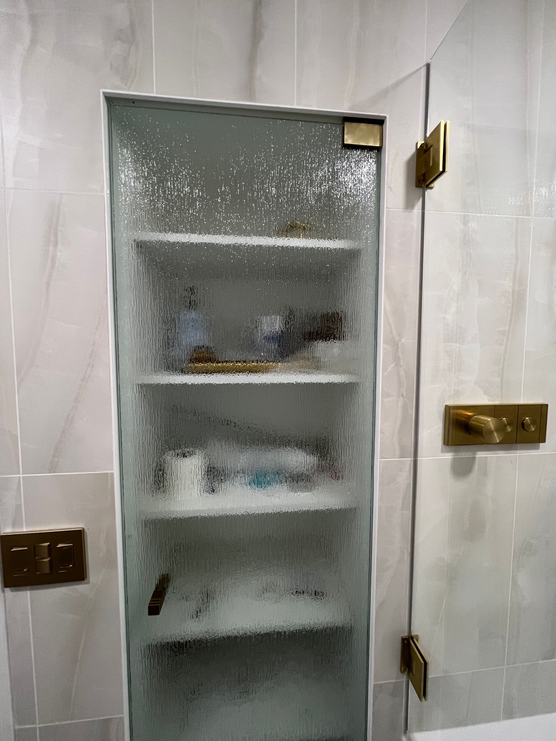 Frosted-glass shower cabinet in a tiled bathroom, with shelves holding toiletries.