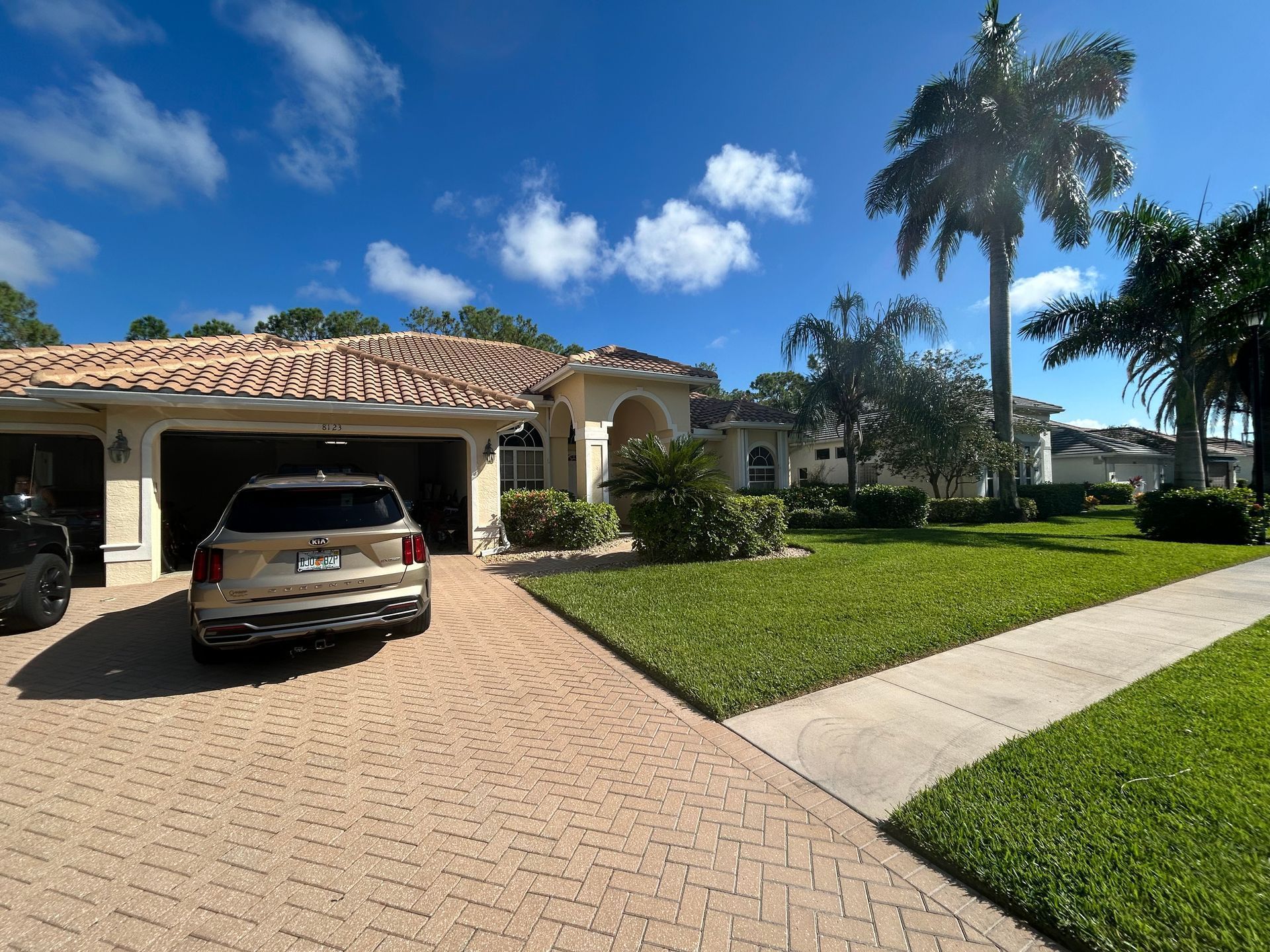 Suburban home with tiled roof, parked SUV in the driveway, palm trees, and a bright blue sky