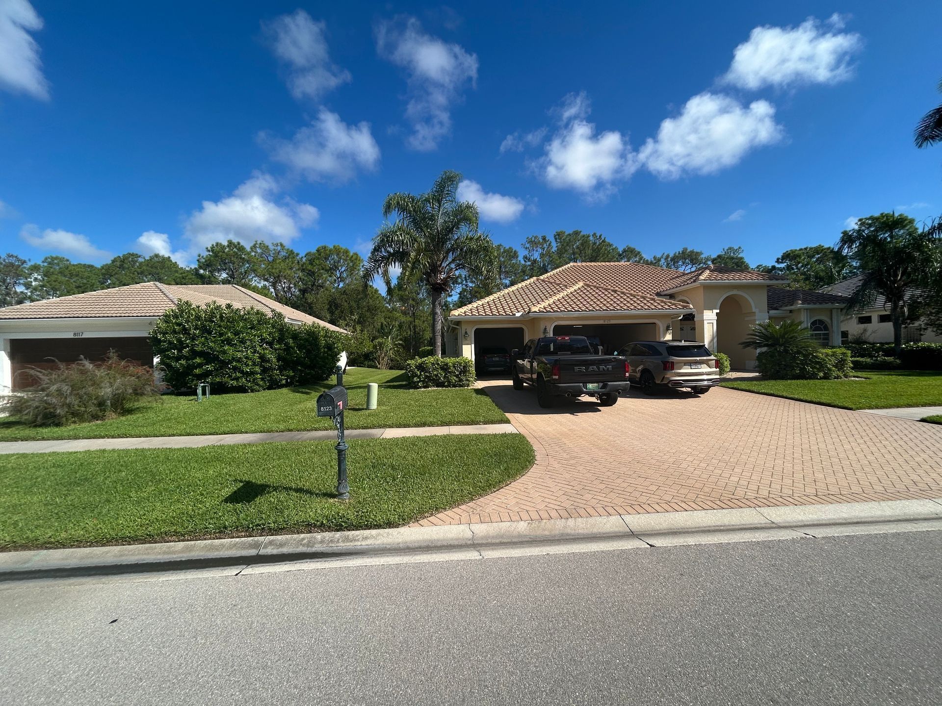 Suburban house with a tiled roof, driveway, and parked cars on a sunny day