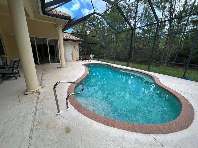 Screened-in backyard pool with curved turquoise water and tan patio beside a house