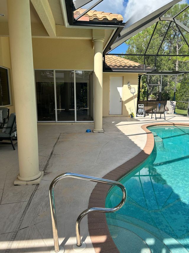 Backyard patio with covered pool, sliding doors, columns, and a metal pool ladder under a glass enclosure.