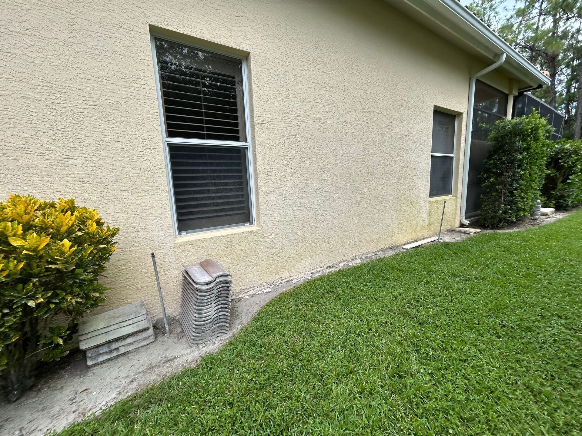 Side of a beige stucco house with two windows, a door, and green lawn along the wall.