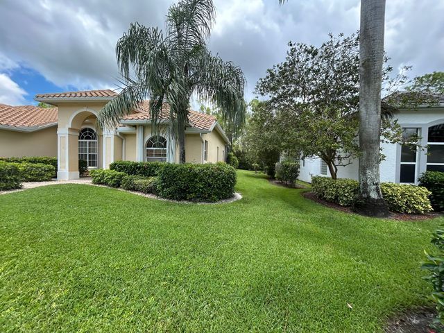 Well-kept suburban house with arched entry, green lawn, palms, and trimmed hedges under a cloudy sky