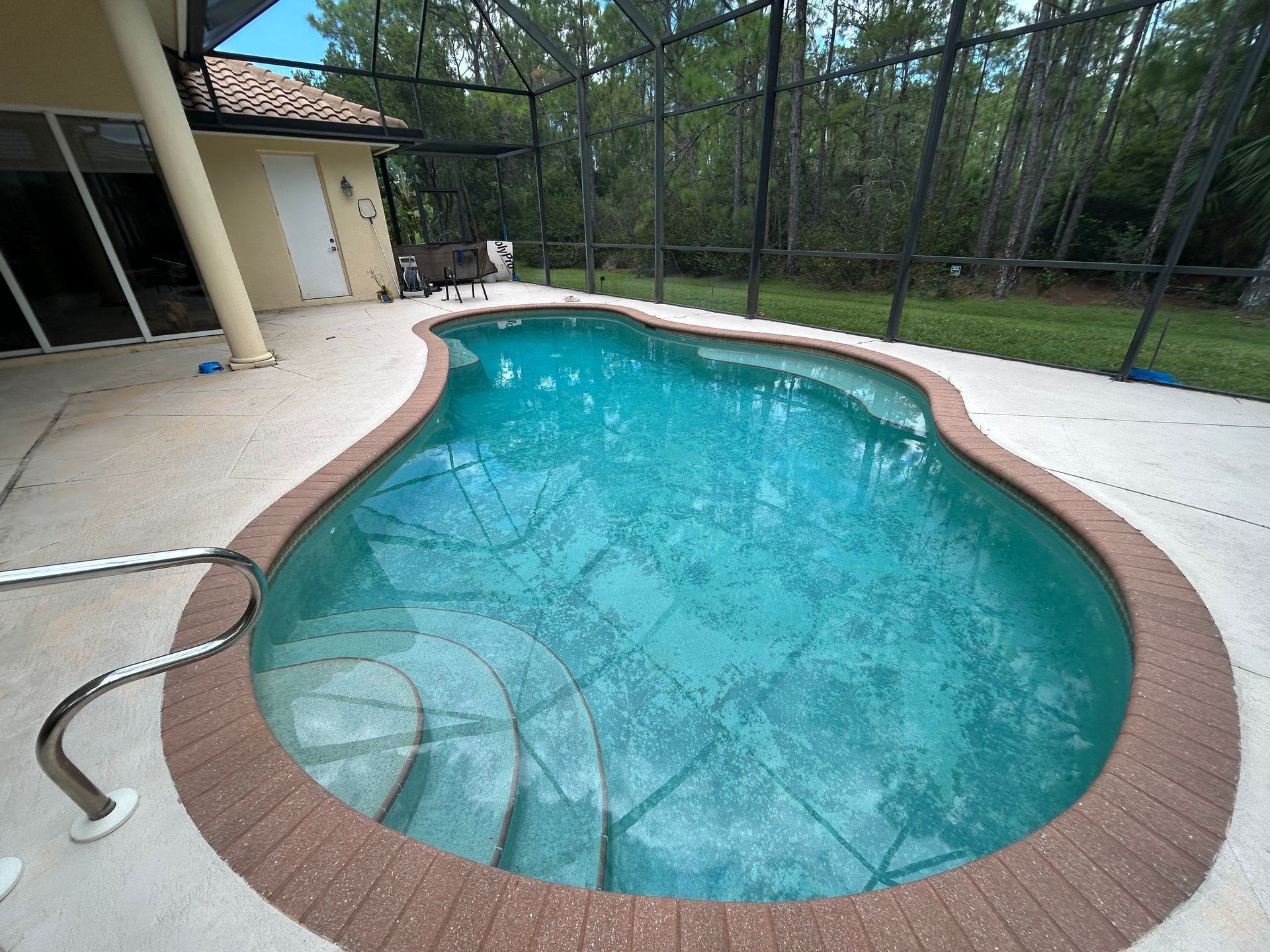 Backyard swimming pool with turquoise water, brick coping, beige deck, and screened enclosure