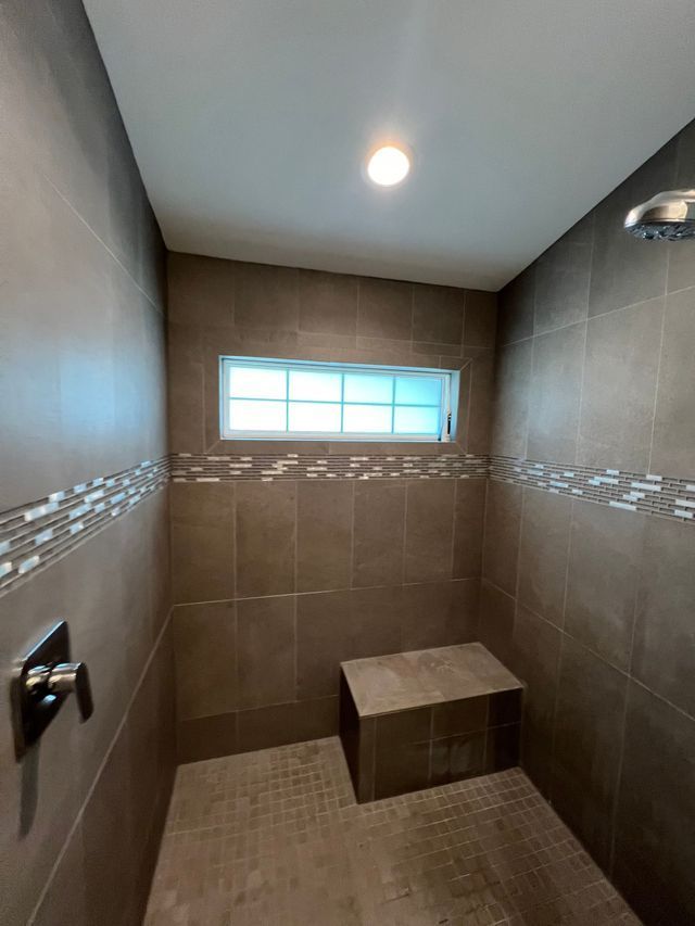 Small tiled shower room with bench, window, and overhead light