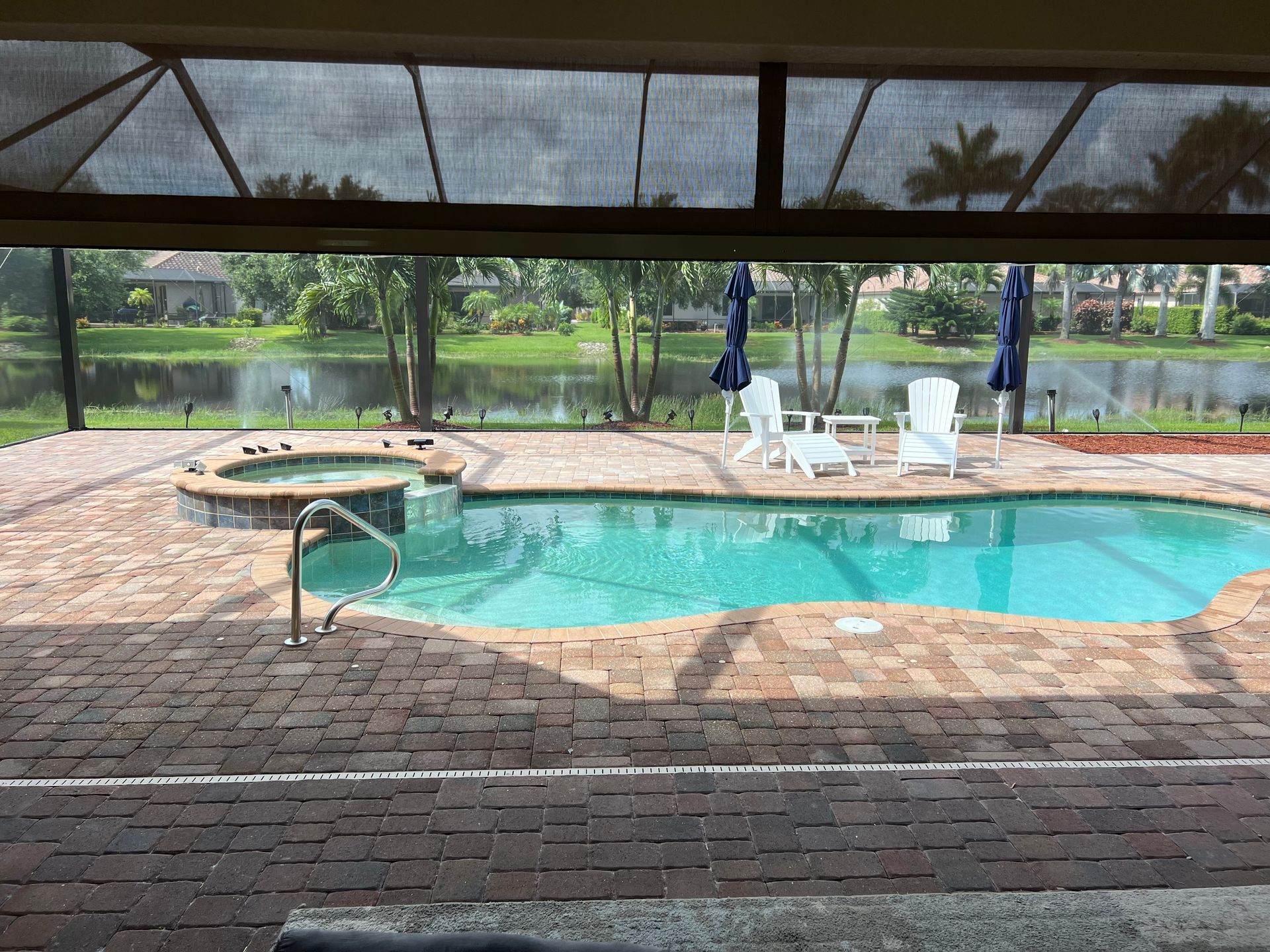 Covered outdoor pool with lounge chairs, brick patio, and screened enclosure overlooking a grassy yard