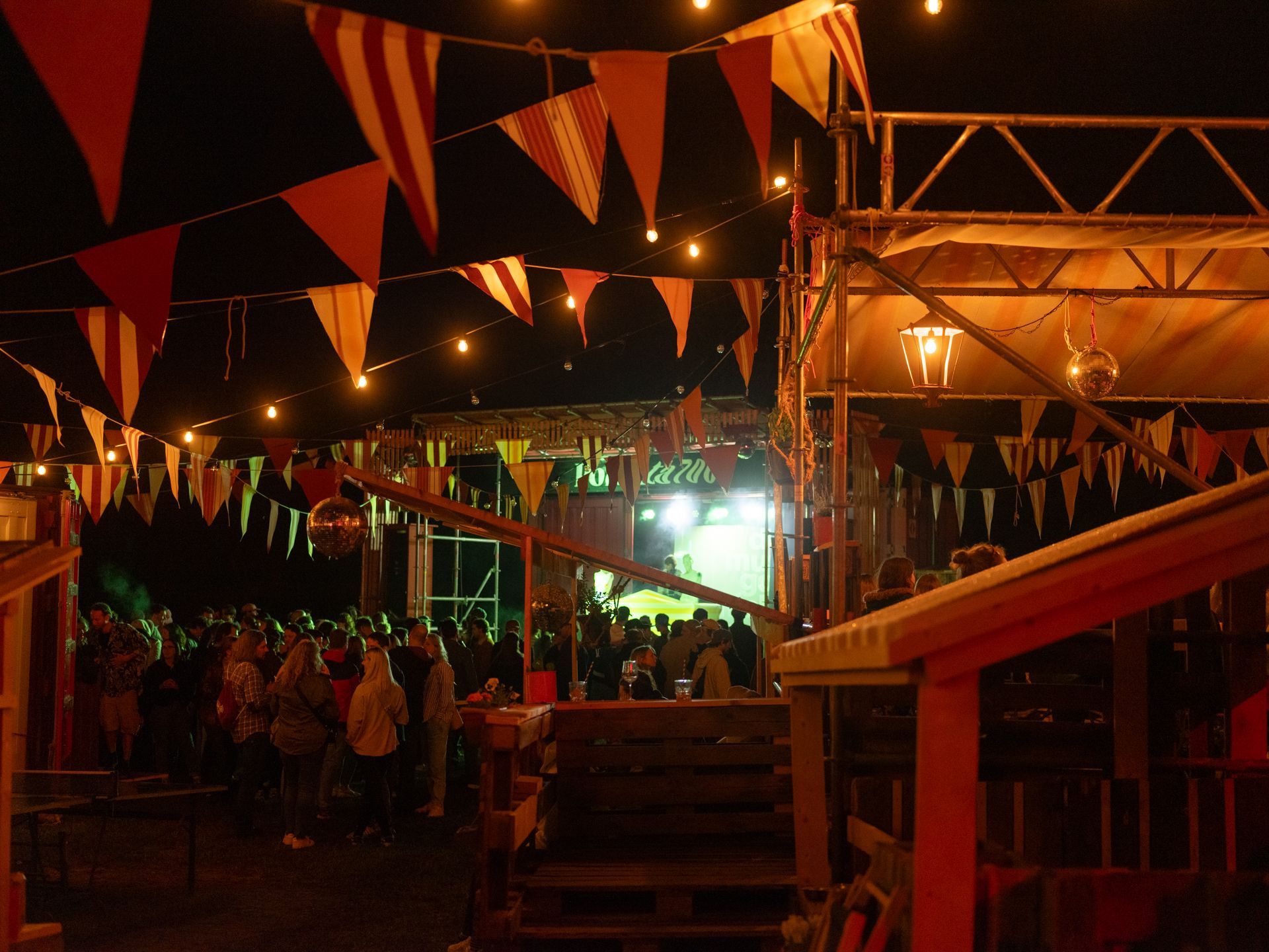 Nighttime outdoor festival with colorful bunting, warm lights, and a crowd near a lit stage