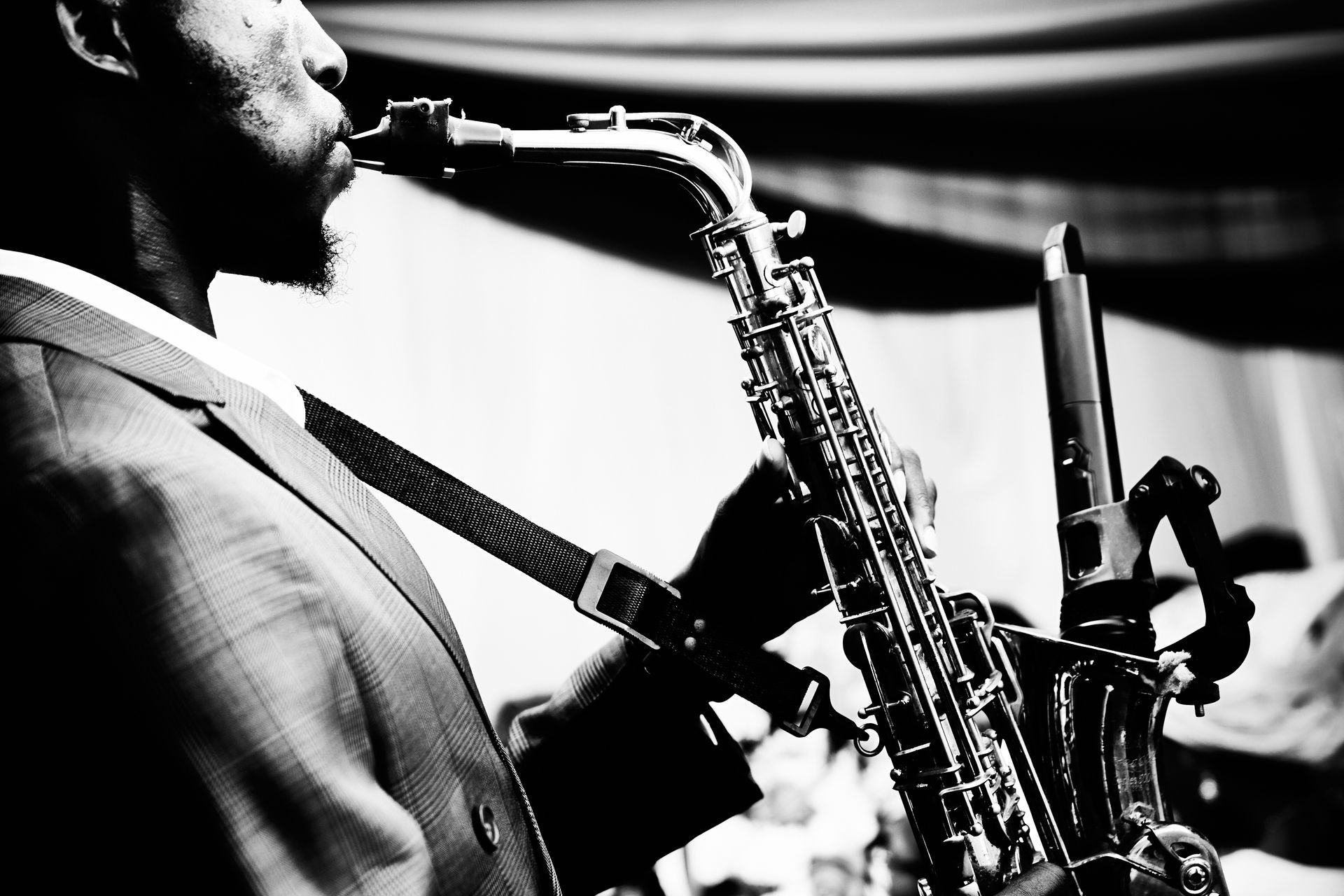 Black-and-white close-up of a saxophonist playing into a microphone on stage